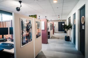 Couloir de bureau moderne avec cloisons modulaires et postes de travail. Design épuré, portes sombres à hublots et affiches "LIEGE DE FRANCE".