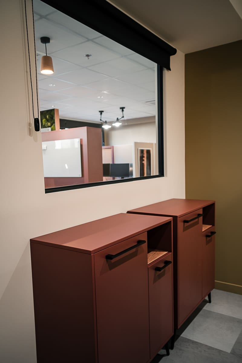 Intérieur de bureau moderne avec deux cabinets de rangement terracotta. Fenêtre intérieure, murs beige et olive. Lumière suspendue en bois.