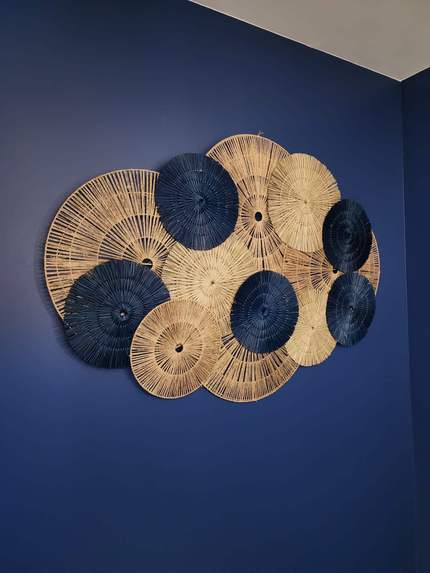 Décoration murale en fibres tressées bleues et naturelles sur mur sombre.