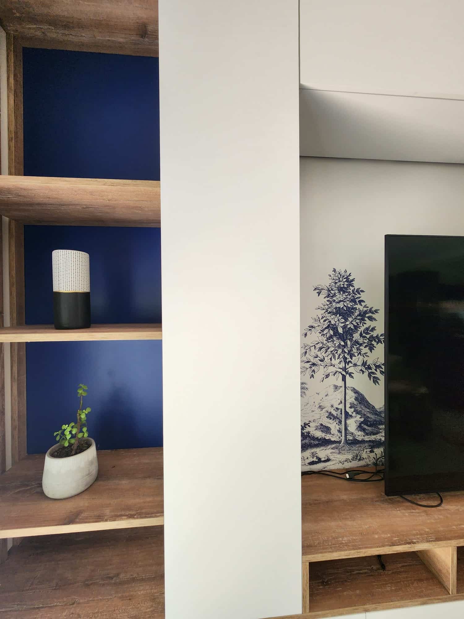 Étagère bois, fond bleu marine avec plante et vase, fresque murale arbre et télévision.