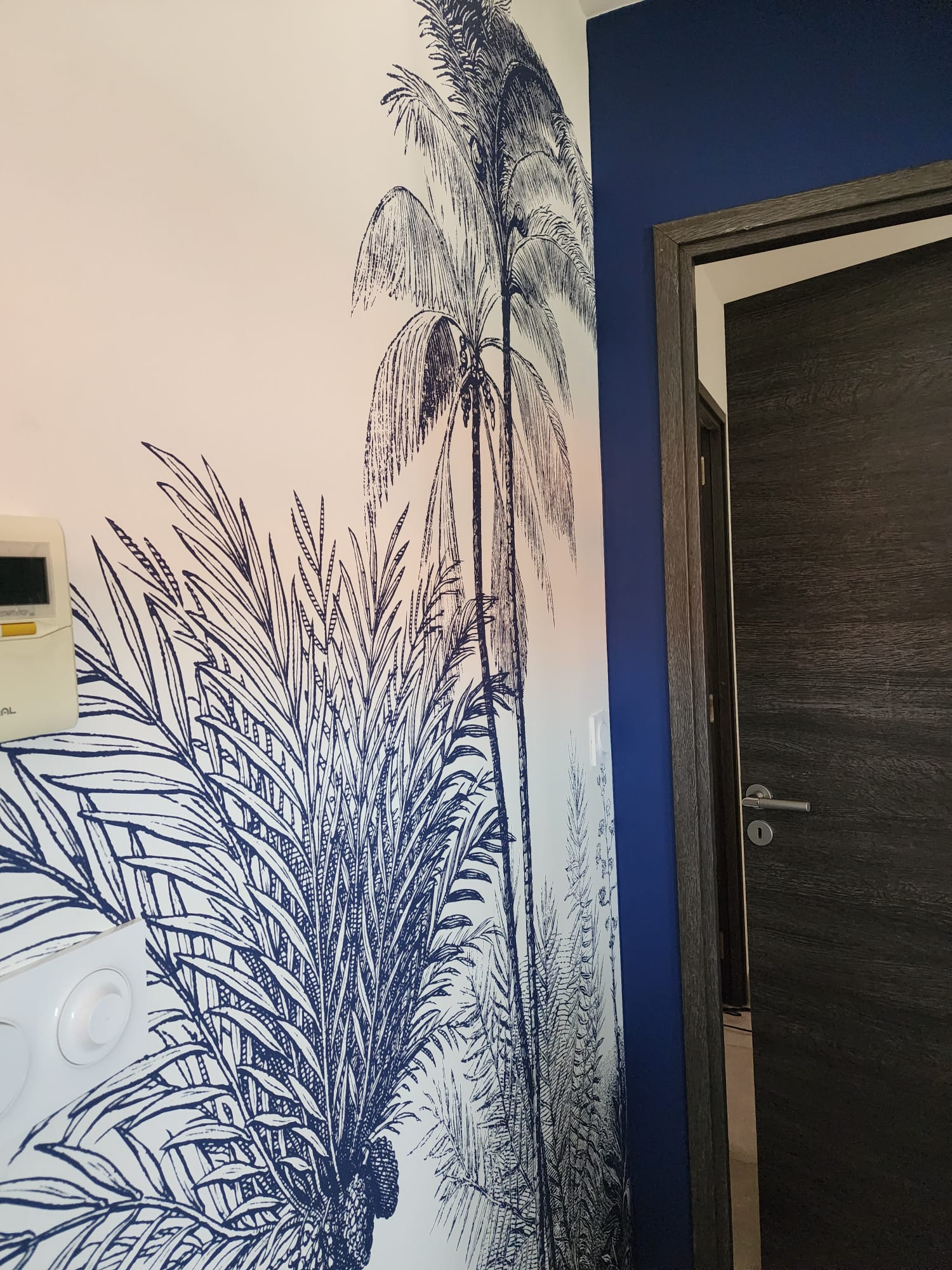 Papier peint tropical bleu et blanc avec palmiers près d'une porte sombre.