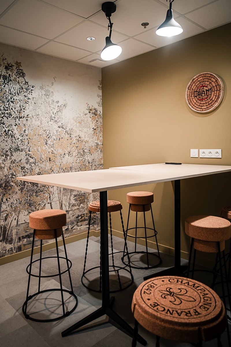 Espace de travail avec table haute et tabourets en liège. Décoration murale "DIAM" et motif forestier. Stool "CHAMPAGNE FRANCE 1842".