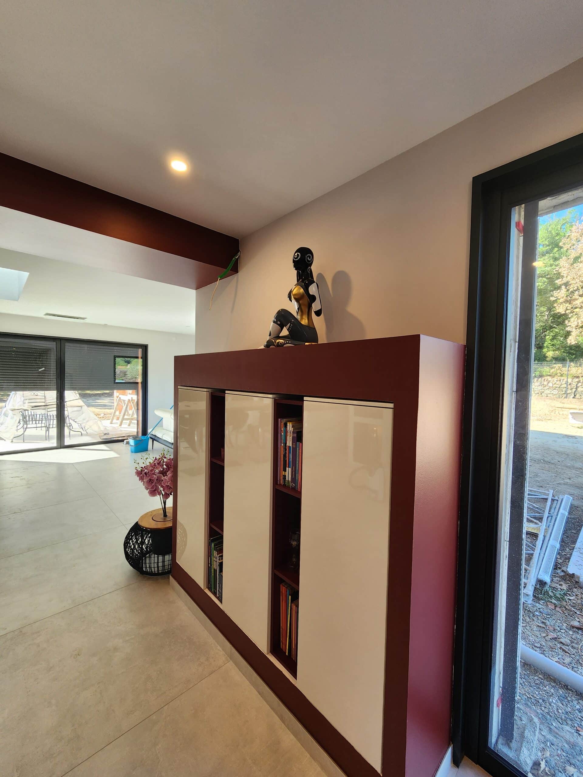 Meuble design bordeaux et blanc avec statuette moderne dans un salon lumineux ouvert sur l'extérieur.