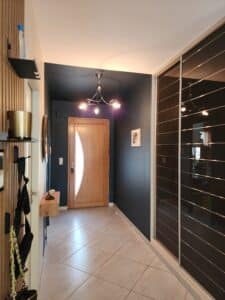 Couloir moderne avec murs bleu nuit, porte en bois clair, lustre chromé et grand placard à miroirs noirs.