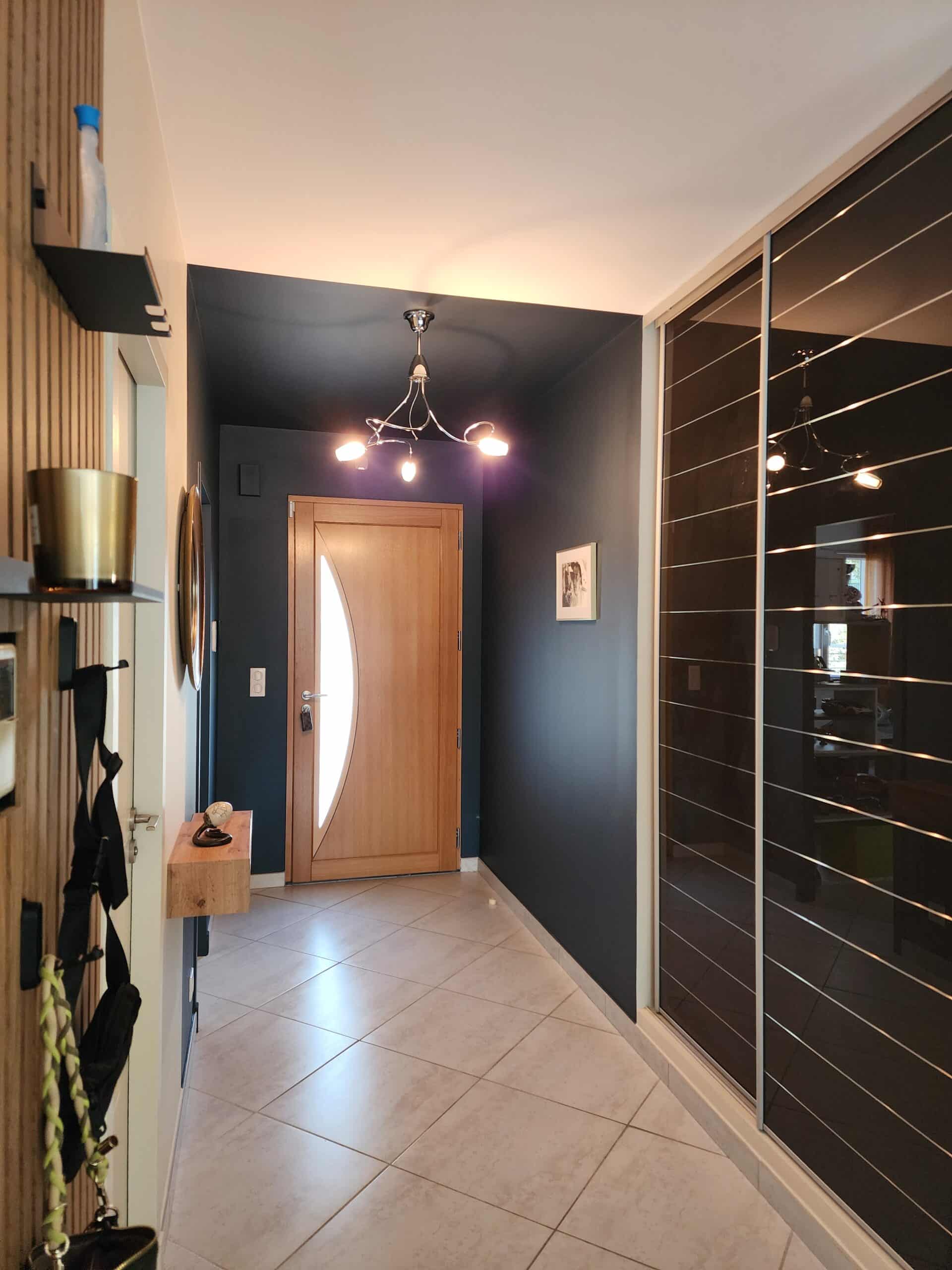 Couloir moderne avec murs bleu nuit, porte en bois clair, lustre chromé et grand placard à miroirs noirs.
