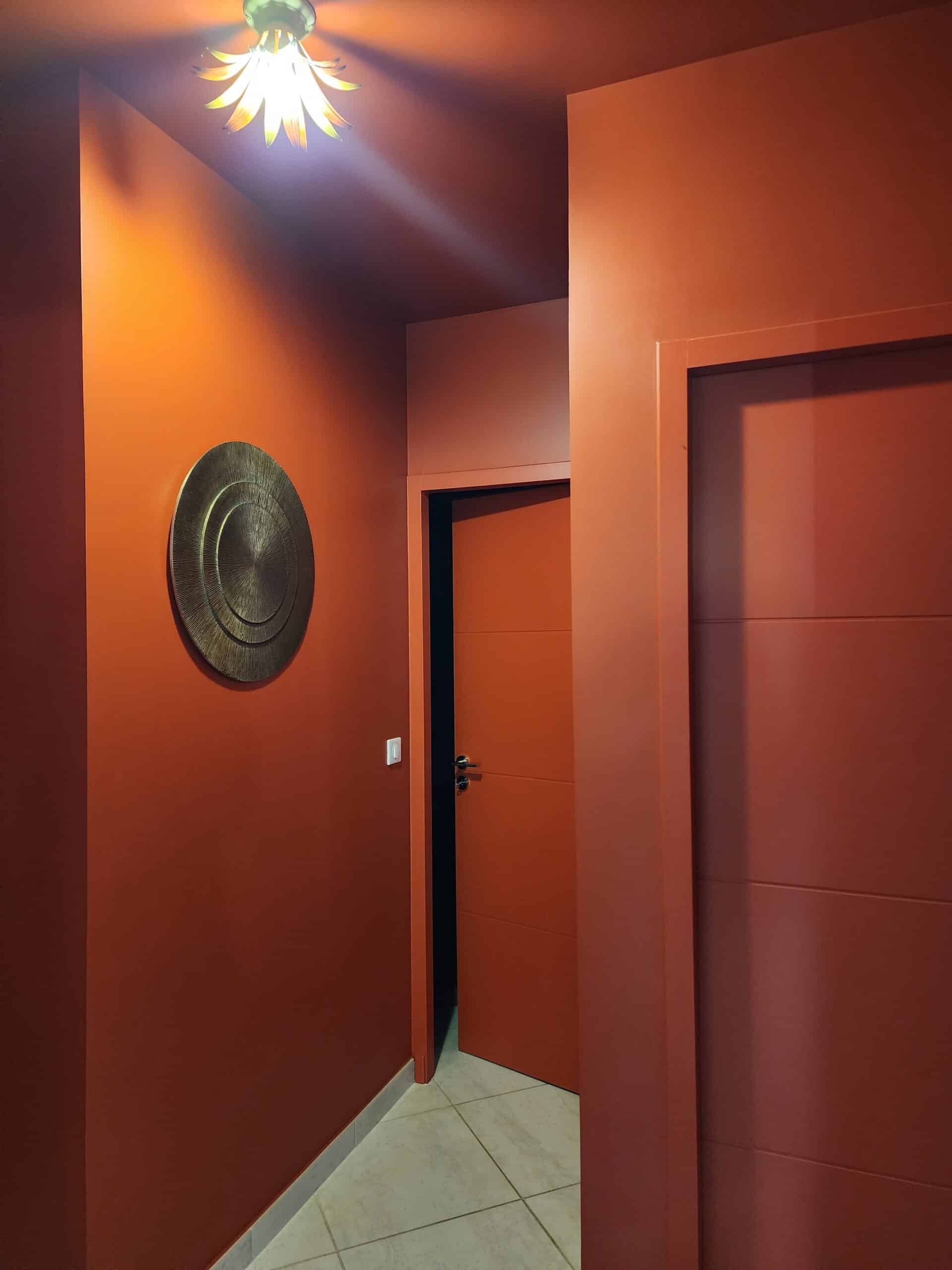 Couloir terracotta moderne, luminaire soleil et décoration murale ronde dorée.