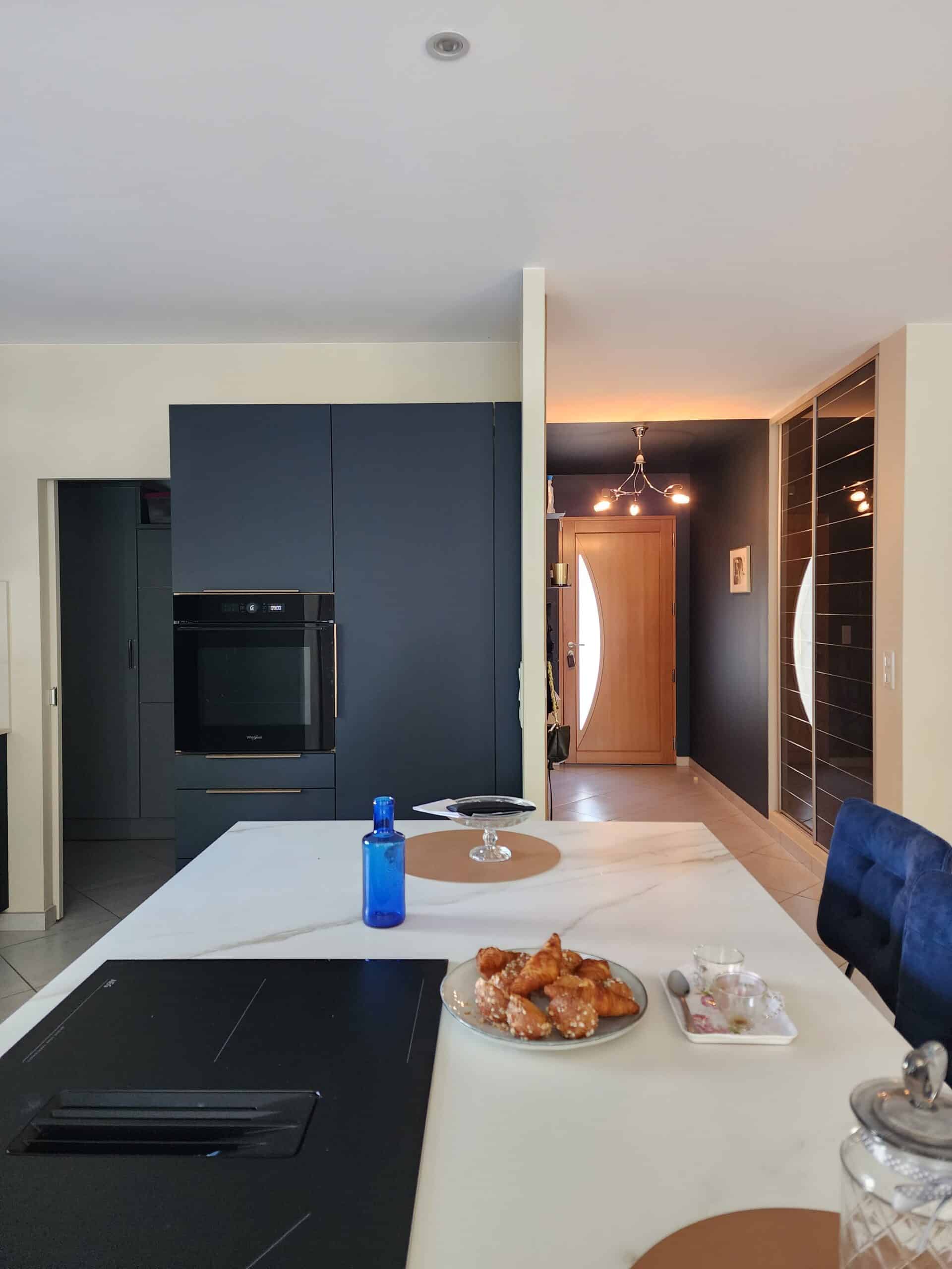 Cuisine moderne : îlot marbre blanc, meubles bleu marine, four encastré et croissants pour le petit-déjeuner.