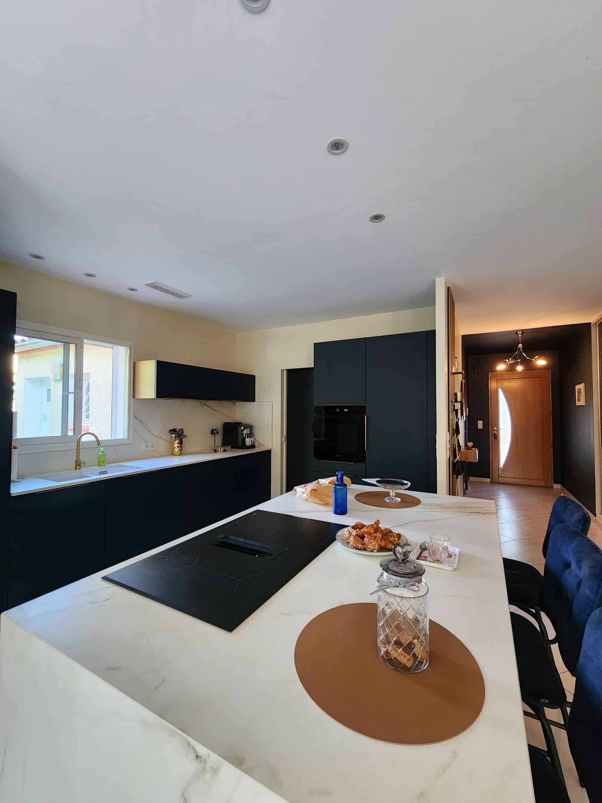 Cuisine moderne aux meubles bleu nuit, îlot marbré blanc et robinet doré.
