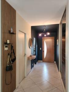 Entrée moderne avec mur en tasseaux de bois, porte en chêne, carrelage clair et luminaire design chaleureux.