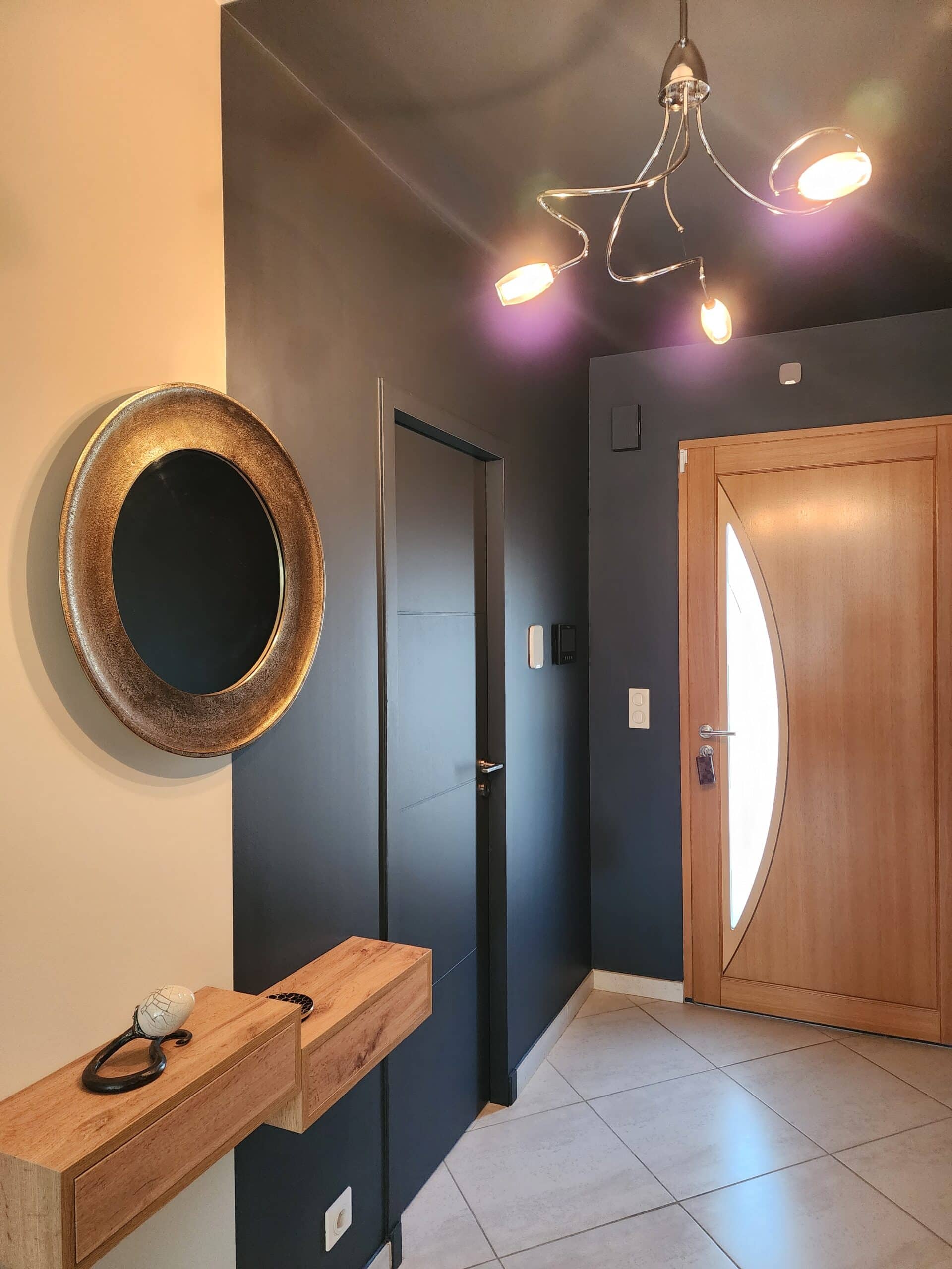 Entrée design : miroir rond doré, console en bois massif et murs gris anthracite.