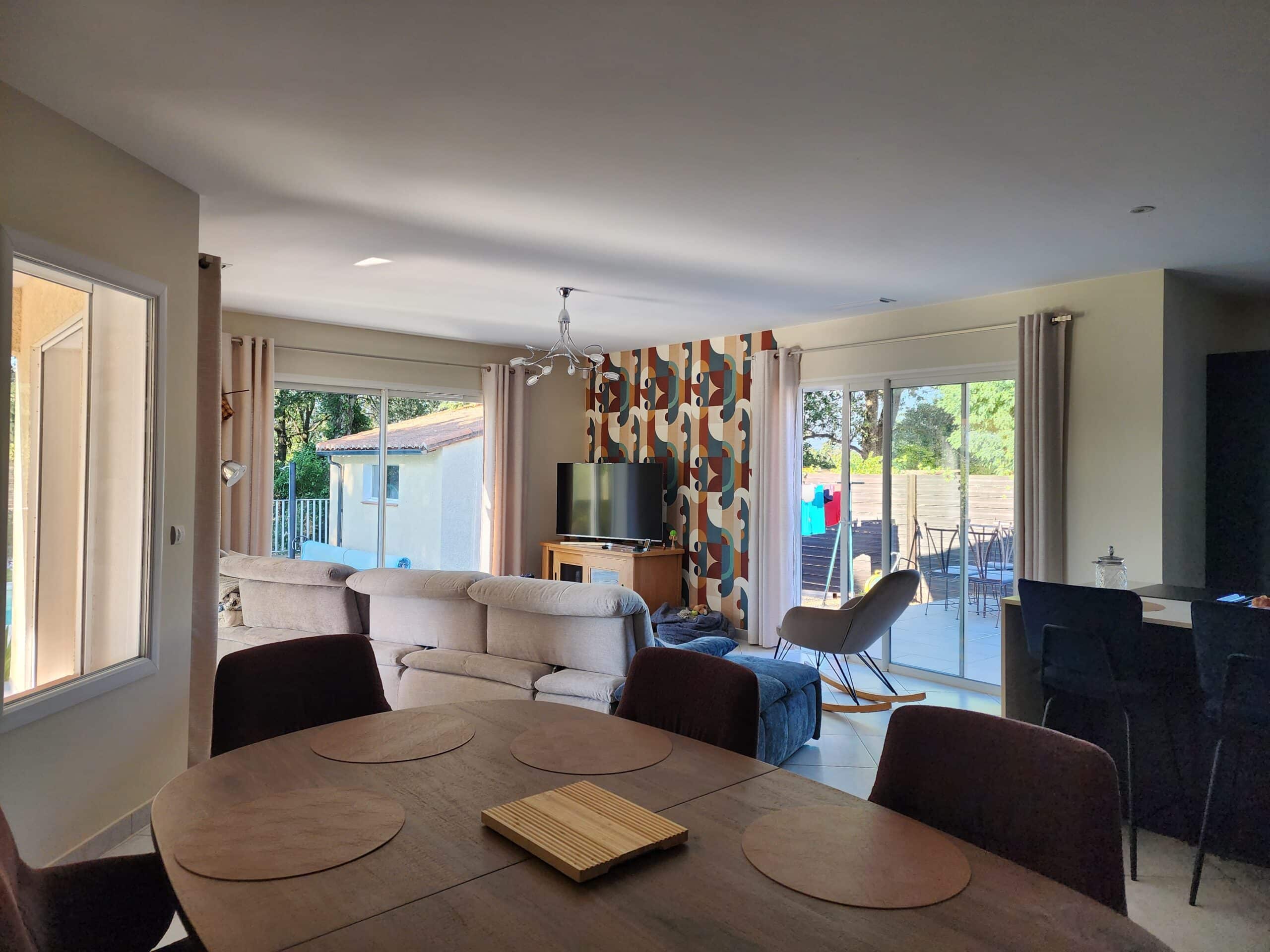 Salon moderne avec table bois, canapé beige et mur coloré ouvrant sur terrasse.