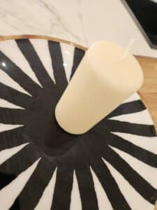 Bougie pilier crème sur un plateau rond à motif rayé noir et blanc, évoquant un style zèbre ou des griffes.