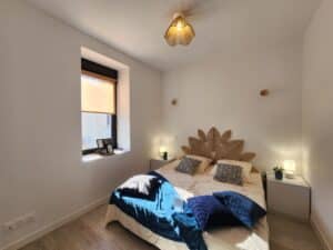 Chambre bohème moderne. Tête de lit en rotin style feuille. Lit double, jeté bleu vif. Note visible: "Merci de ne pas s'asseoir. Fragile."