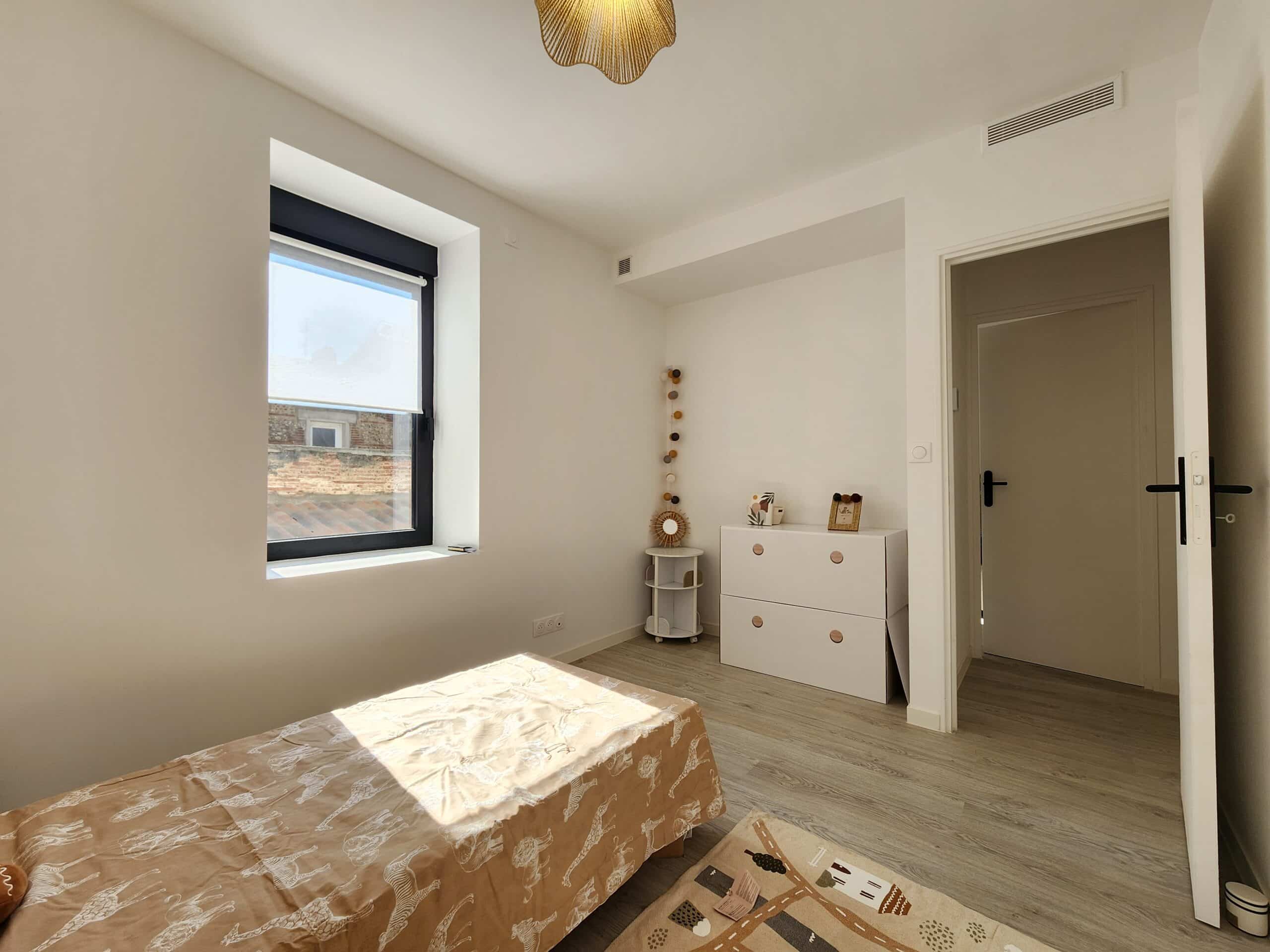 Chambre enfant lumineuse. Lit parure safari éclairé par la fenêtre noire. Commode blanche, parquet gris clair et décoration minimaliste.