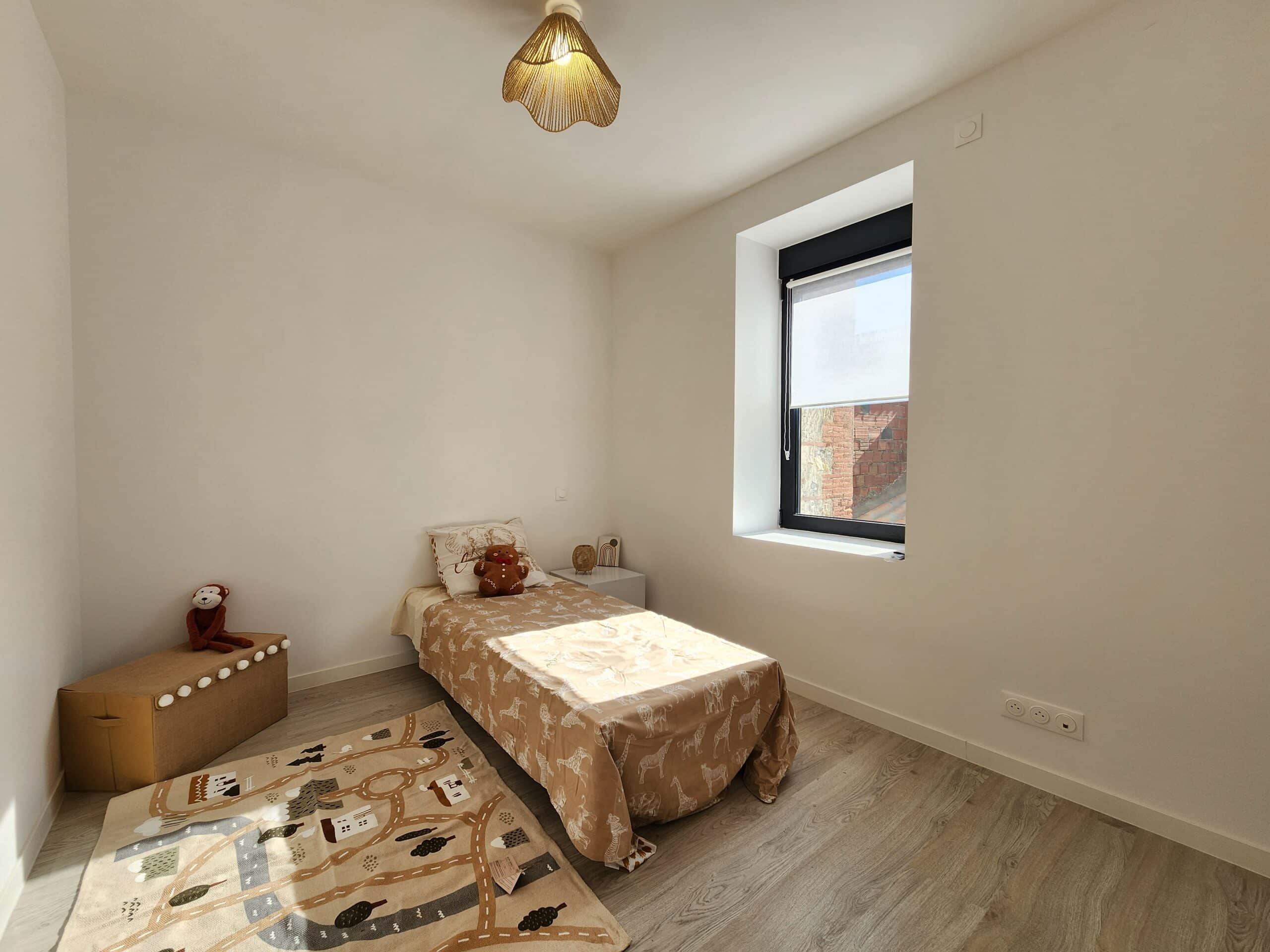 Chambre d'enfant minimaliste et lumineuse. Murs blancs, plancher en bois clair, lit safari brun, tapis de jeu et suspension en corde.