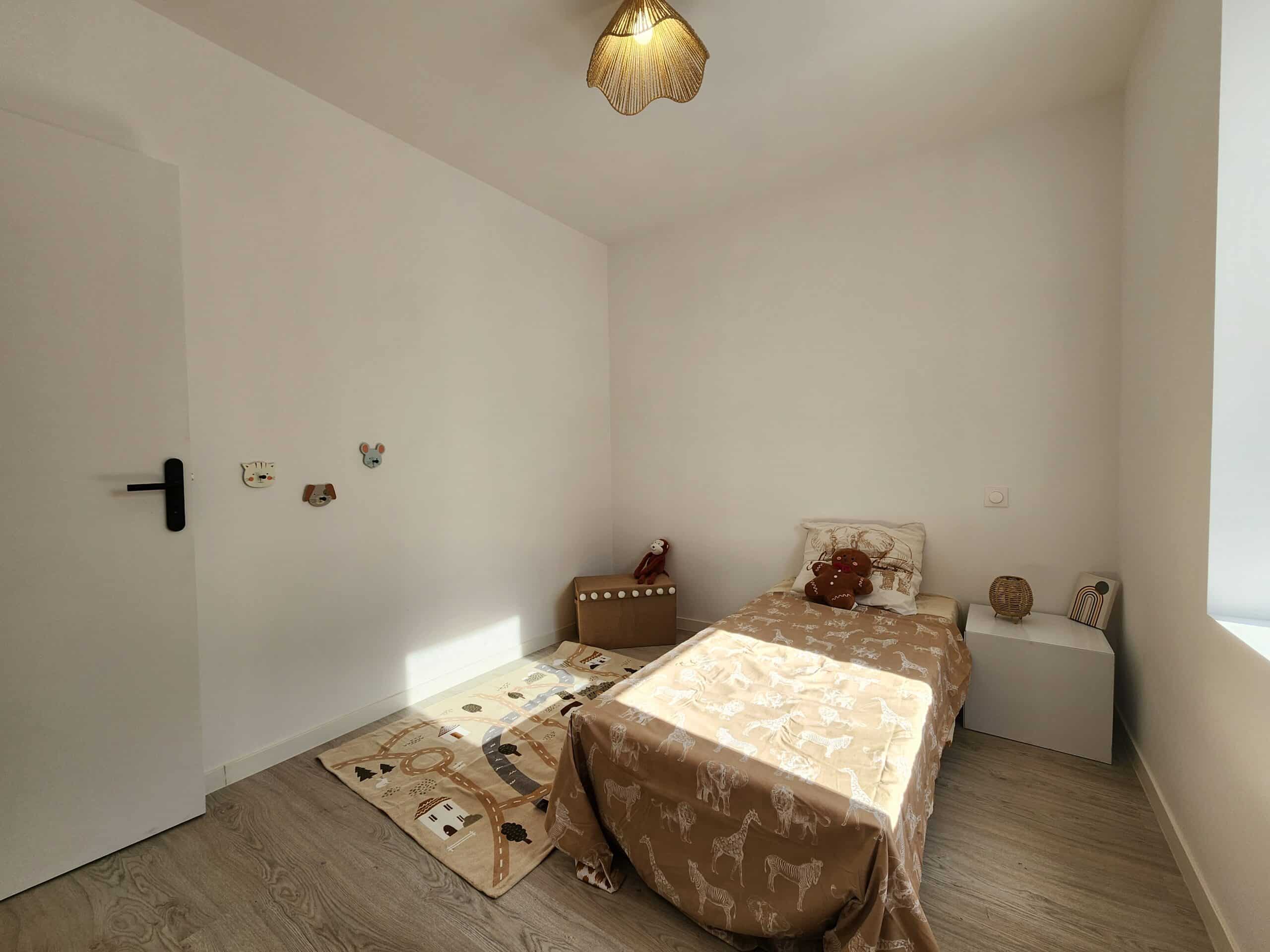 Chambre enfant lumineuse. Décoration minimaliste beige safari : lit animaux, tapis de jeu routes et luminaires osier.