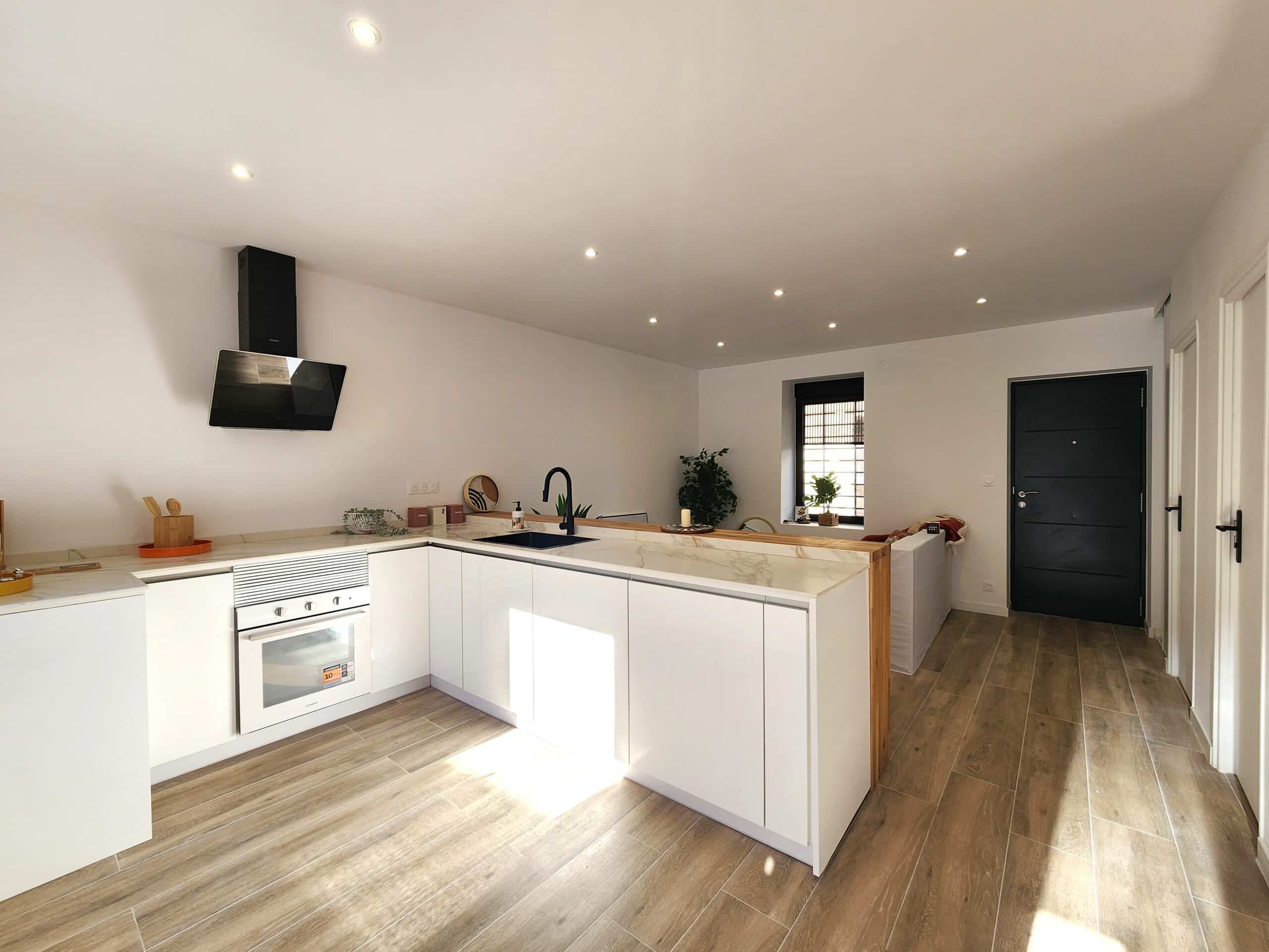 Cuisine ouverte blanche et moderne avec îlot central, comptoir effet marbre et détails bois. Sol carrelé imitation bois.