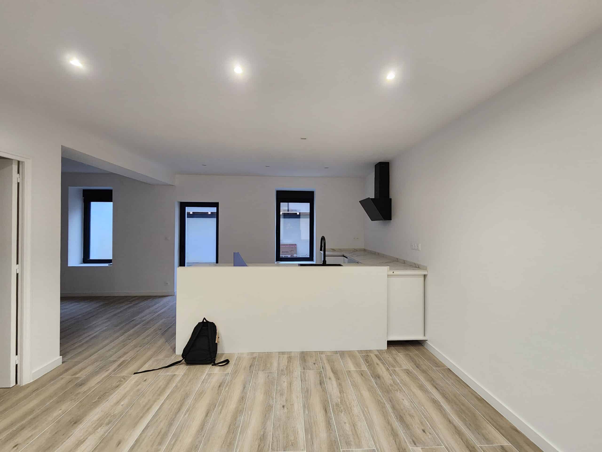Intérieur moderne et lumineux. Cuisine ouverte minimaliste avec îlot blanc, hotte design noire. Sol carrelage imitation bois.