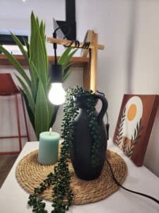 Décoration de table bohème: vase noir, plante succulente, bougie menthe, et lampe minimaliste en bois sur napperon tressé.