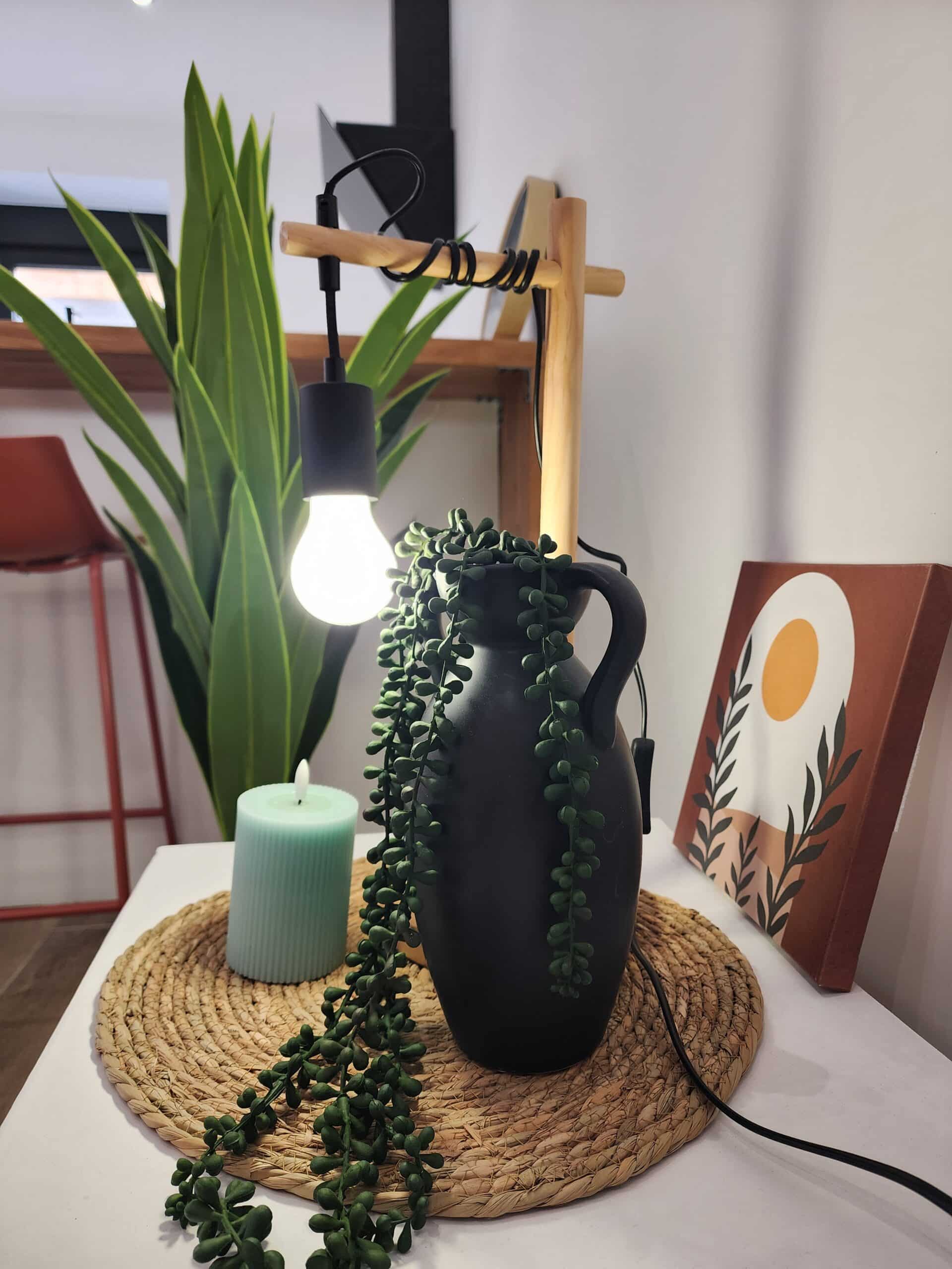 Décoration de table bohème: vase noir, plante succulente, bougie menthe, et lampe minimaliste en bois sur napperon tressé.