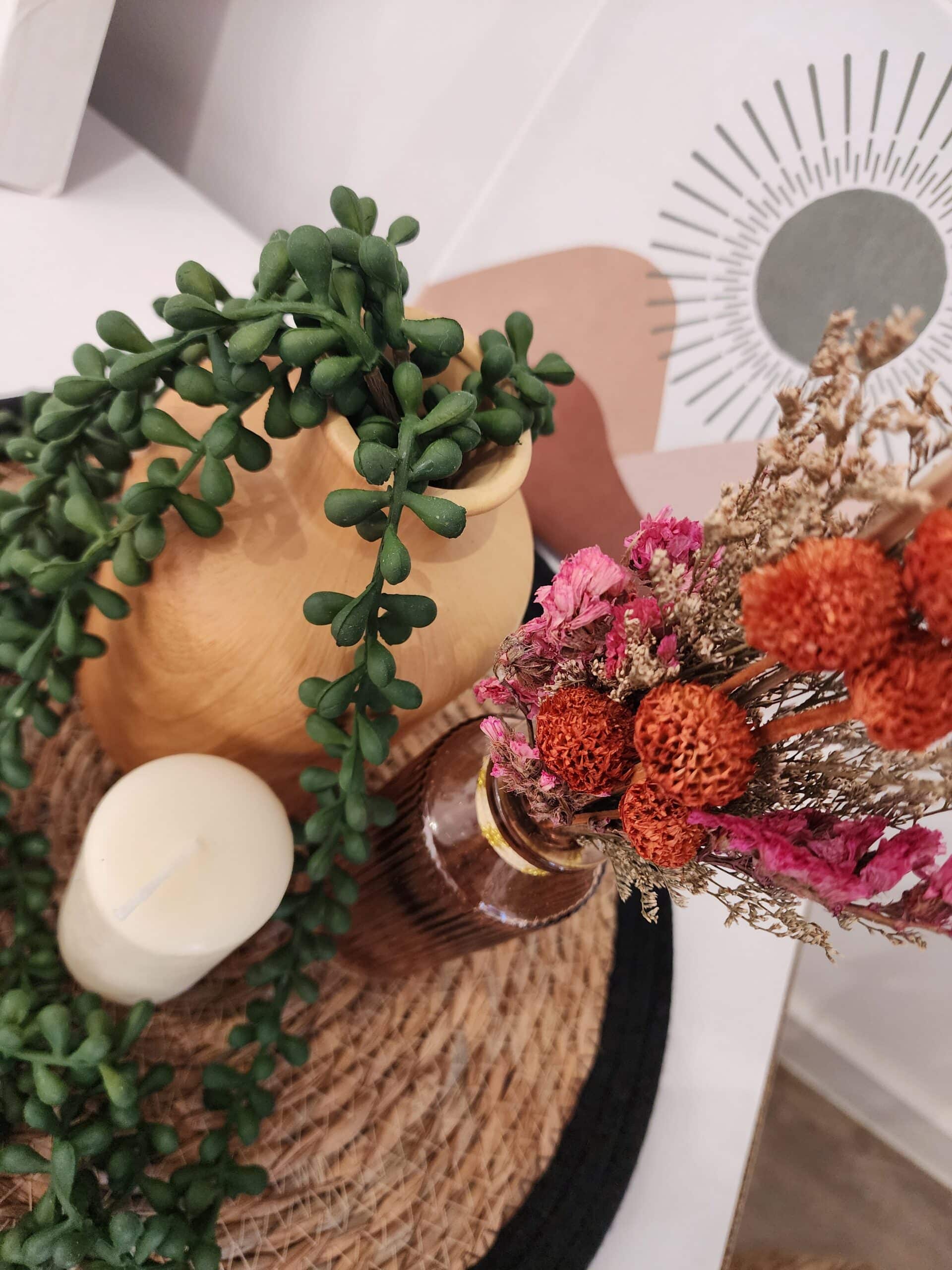 Composition décorative bohème: vase en bois, fausse succulente retombante, bougie blanche et fleurs séchées sur napperon tressé. Art abstrait soleil.