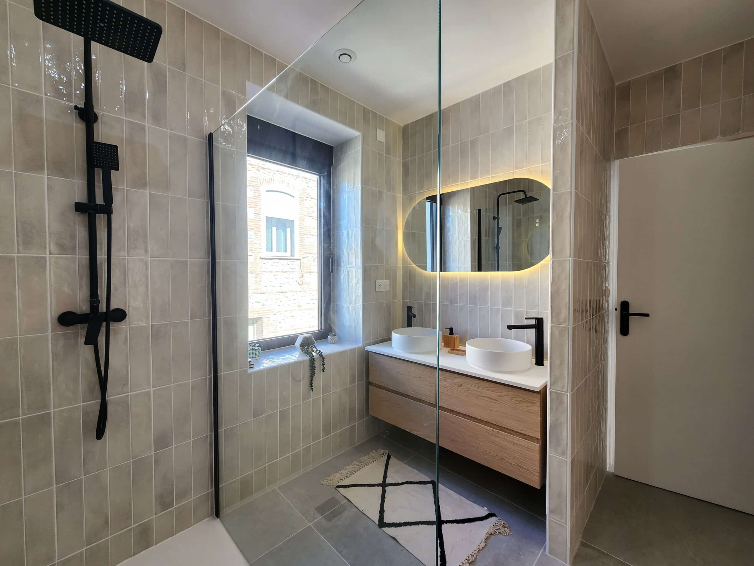 Design moderne : douche italienne, carrelage vertical beige, double vasque bois/blanc, miroir lumineux et robinetterie noire mate.