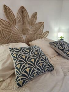 Chambre style bohème. Tête de lit feuilles en jute tressé. Lit blanc, coussins bleu canard et or à motif éventail.