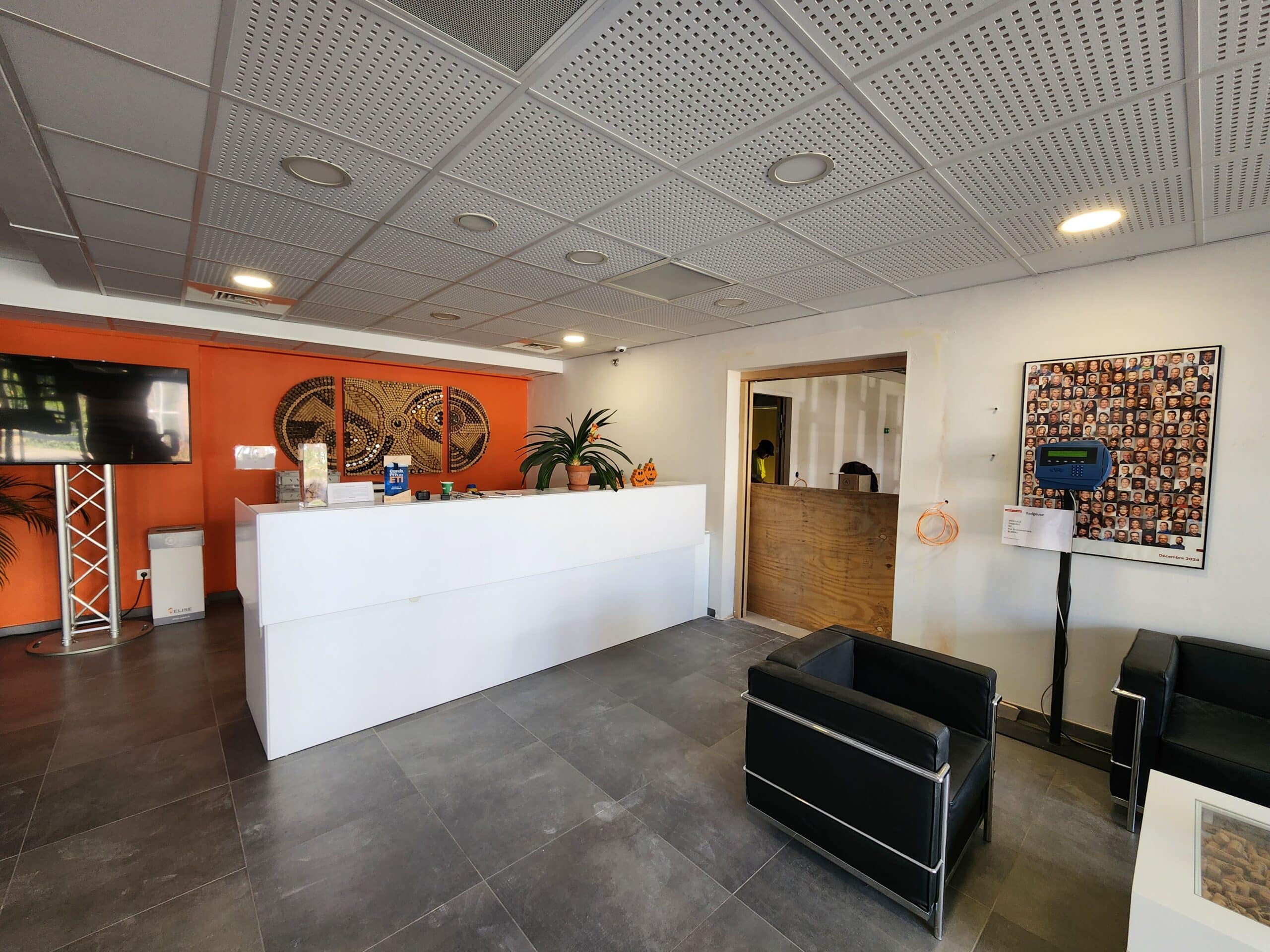 Accueil moderne avec comptoir blanc, mur orange, fauteuil noir et décoration murale. Espace de réception d'entreprise.