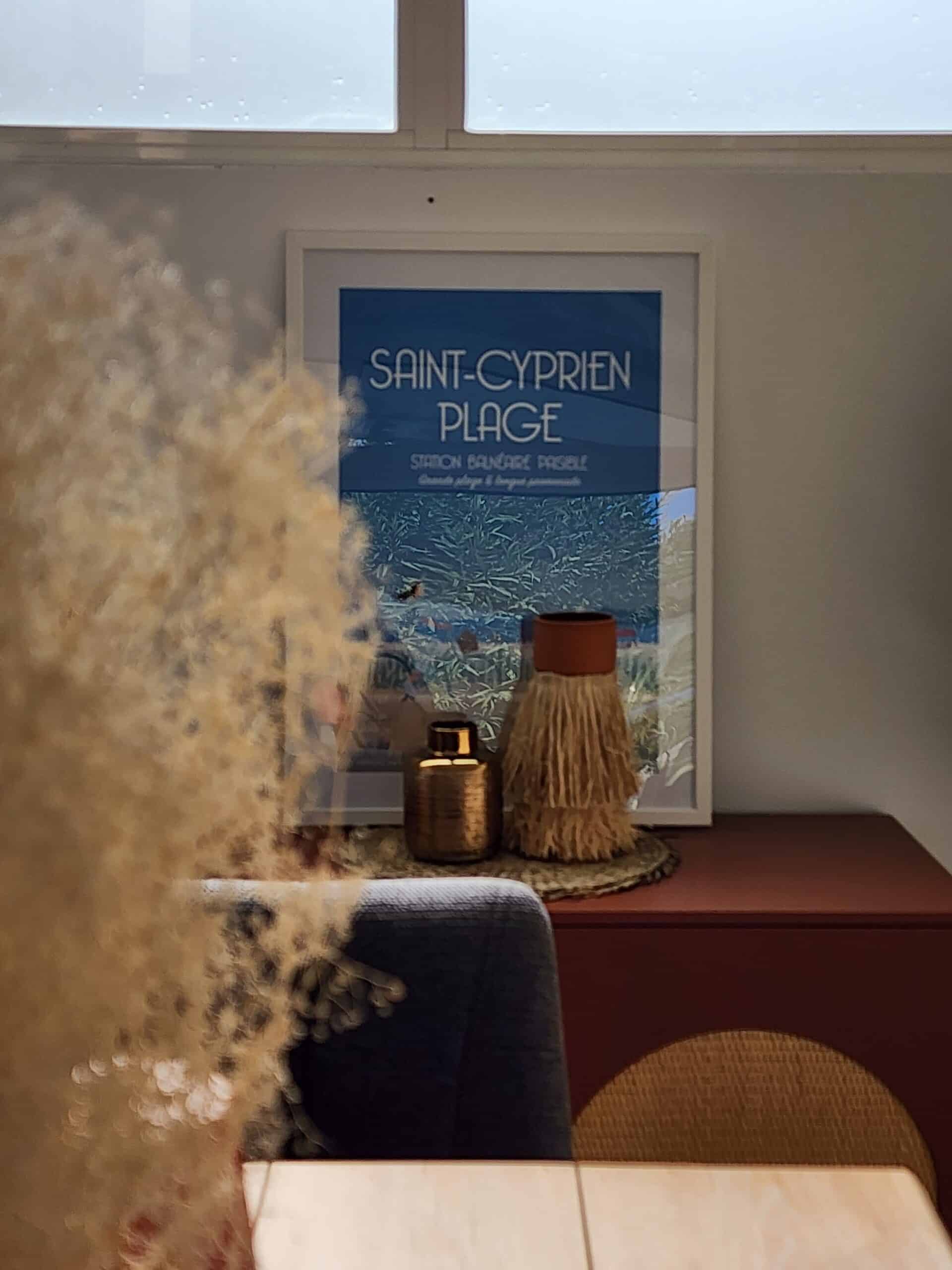 Affiche Saint-Cyprien Plage, vases dorés et à franges sur buffet avec fleurs séchées au premier plan.