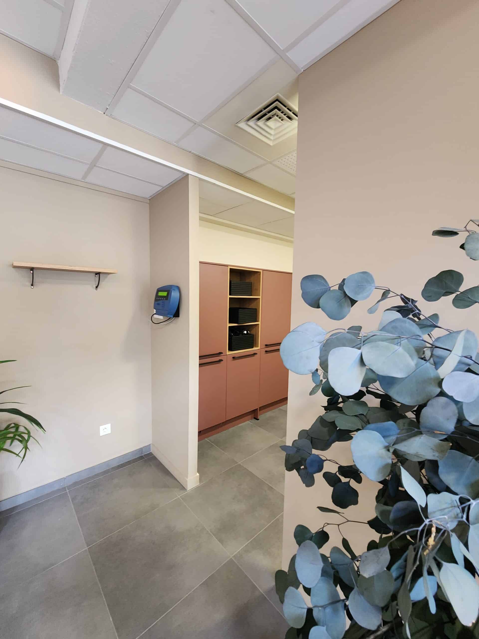 Pointeuse bleue, étagère en bois et placards terracotta dans un bureau moderne.