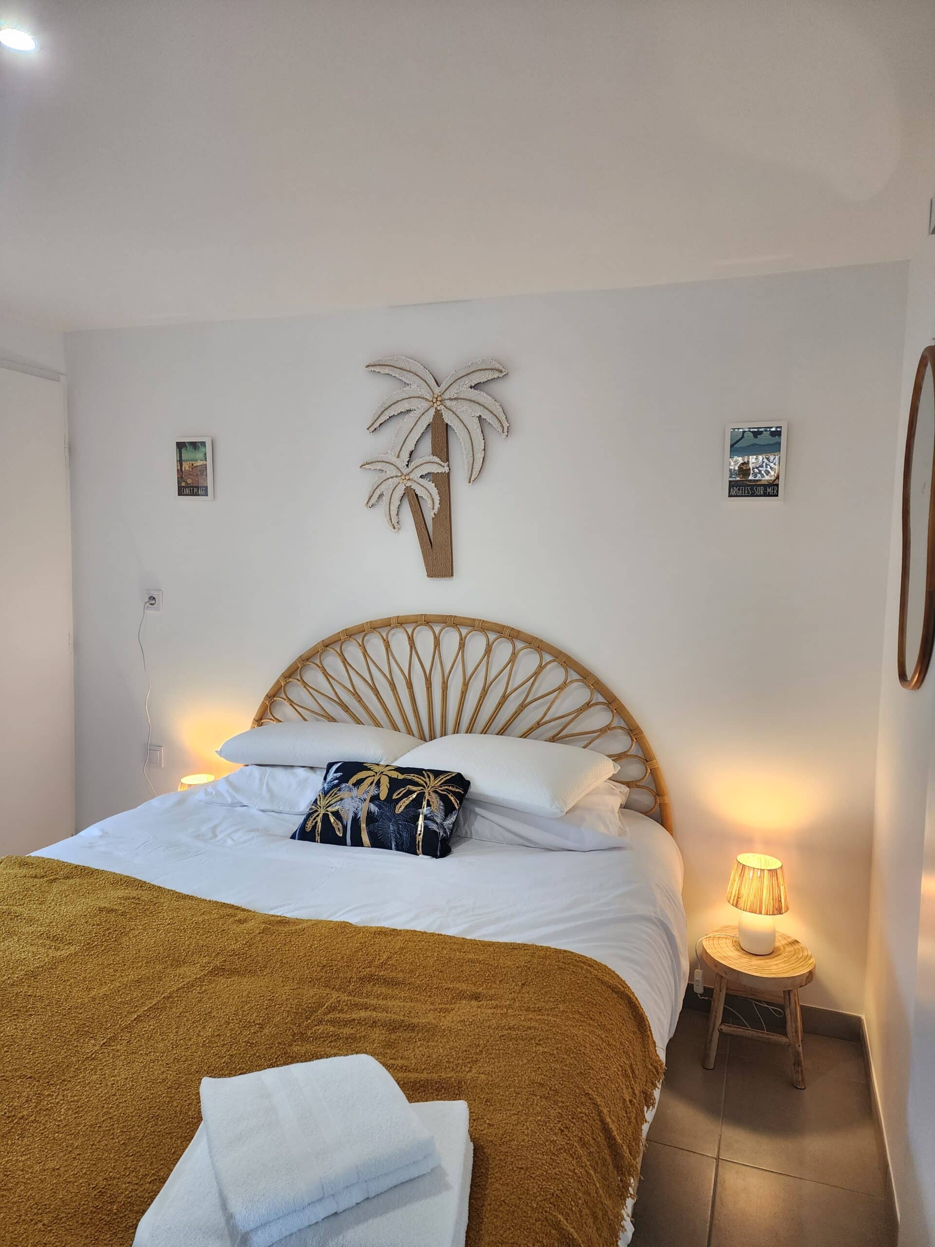 Chambre bohème avec lit en rotin, plaid moutarde, décor palmier et affiches Argelès-sur-Mer et Canet Plage.