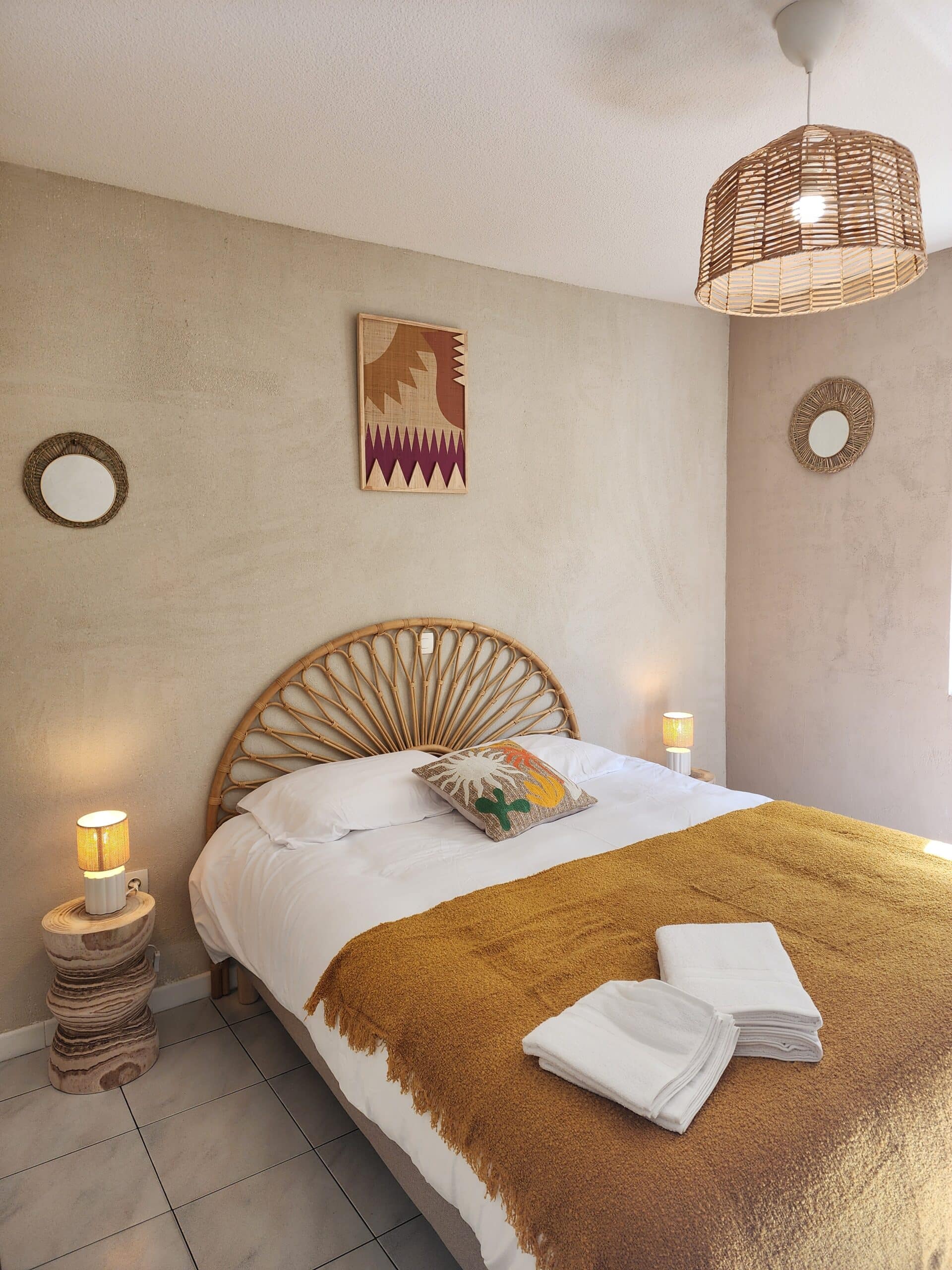 Chambre bohème avec tête de lit en rotin, jeté moutarde et luminaires naturels.