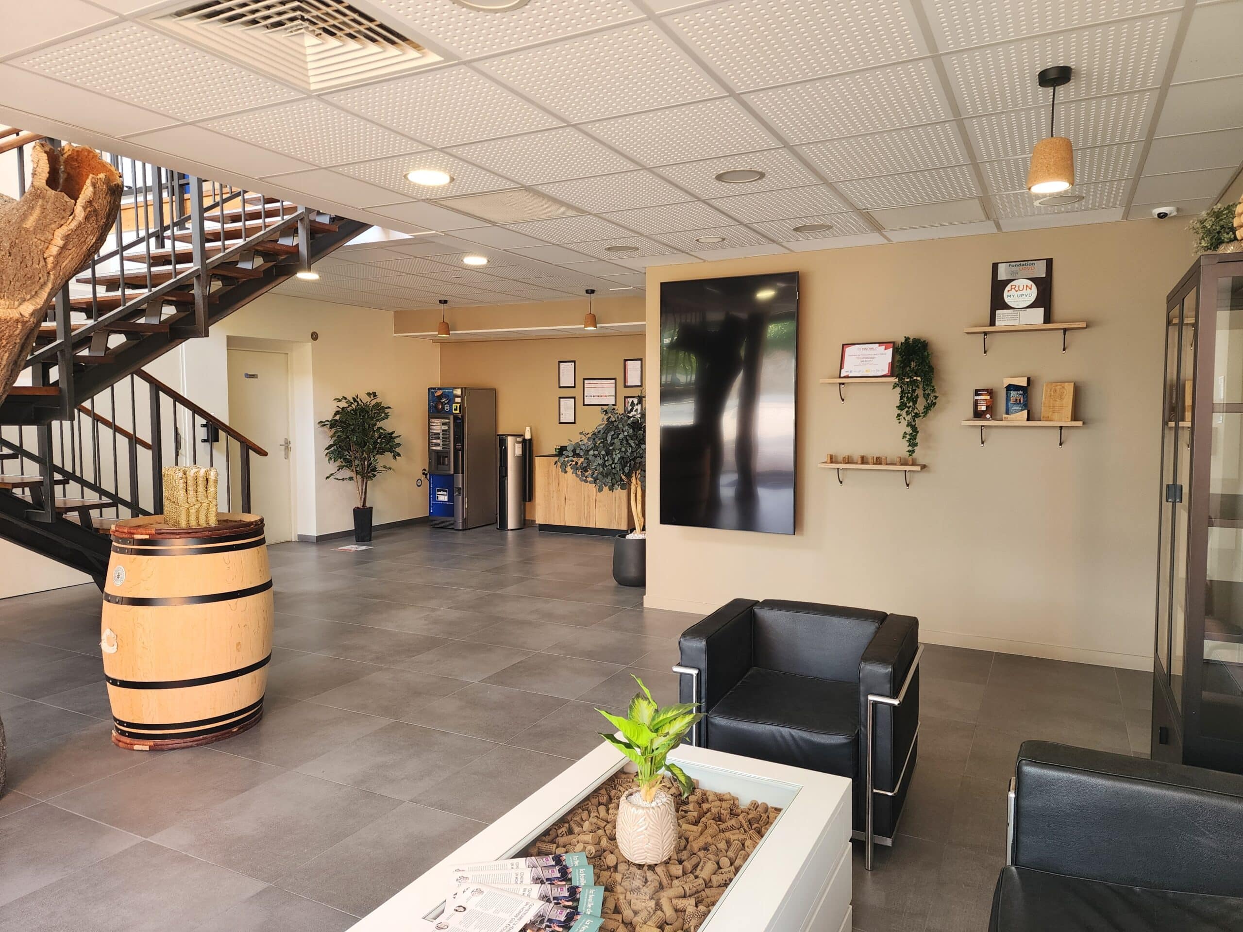 Hall d'accueil moderne avec fauteuils en cuir noir, tonneau décoratif et table basse remplie de bouchons de liège.