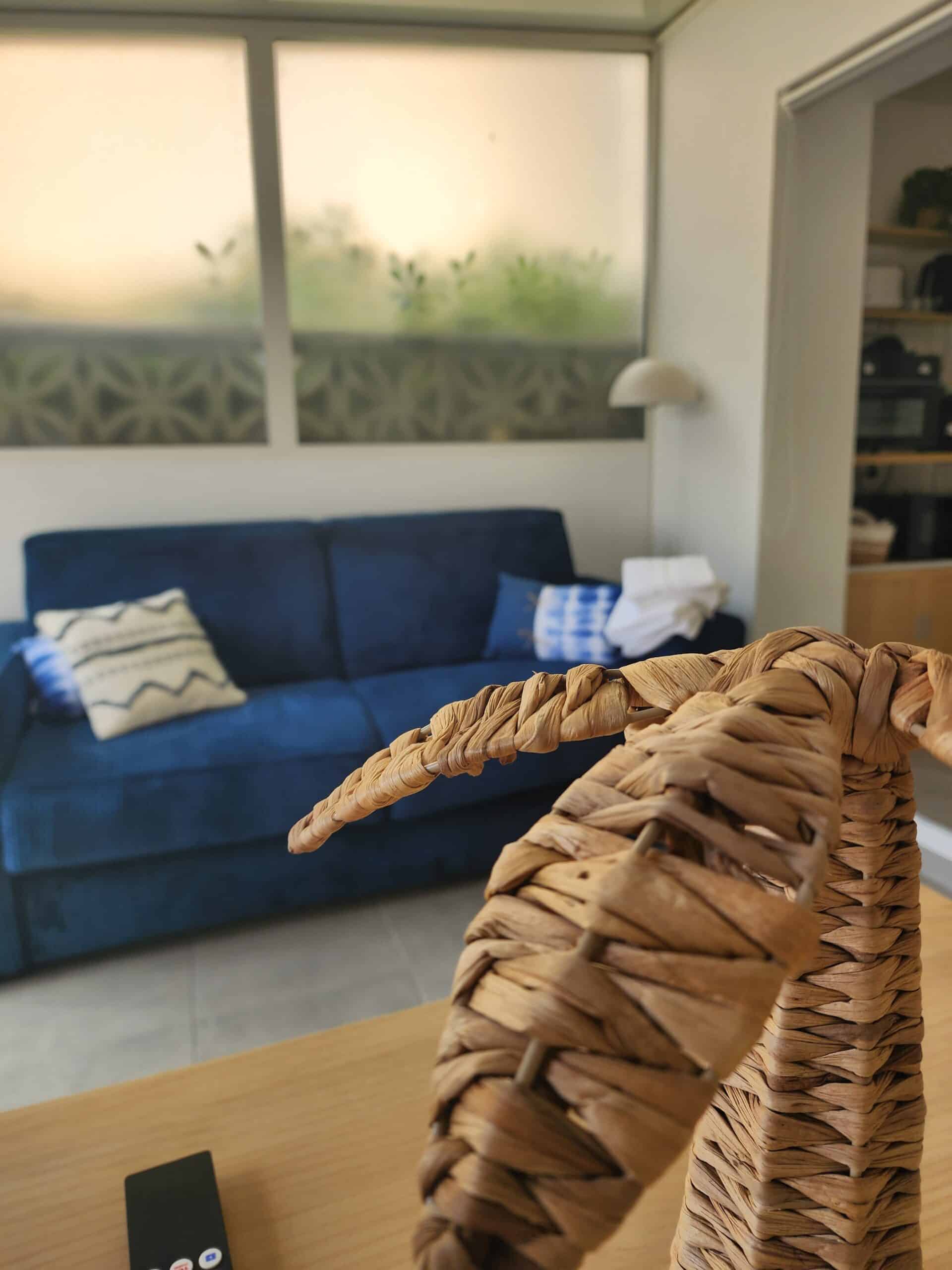 Palmier tressé en osier au premier plan devant un canapé bleu et des coussins.