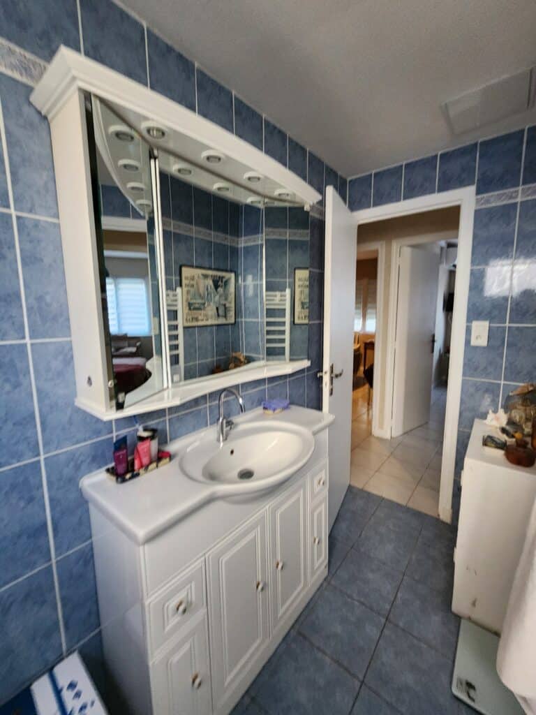Salle de bain à carrelage bleu avec meuble vasque blanc et armoire de toilette à miroir.