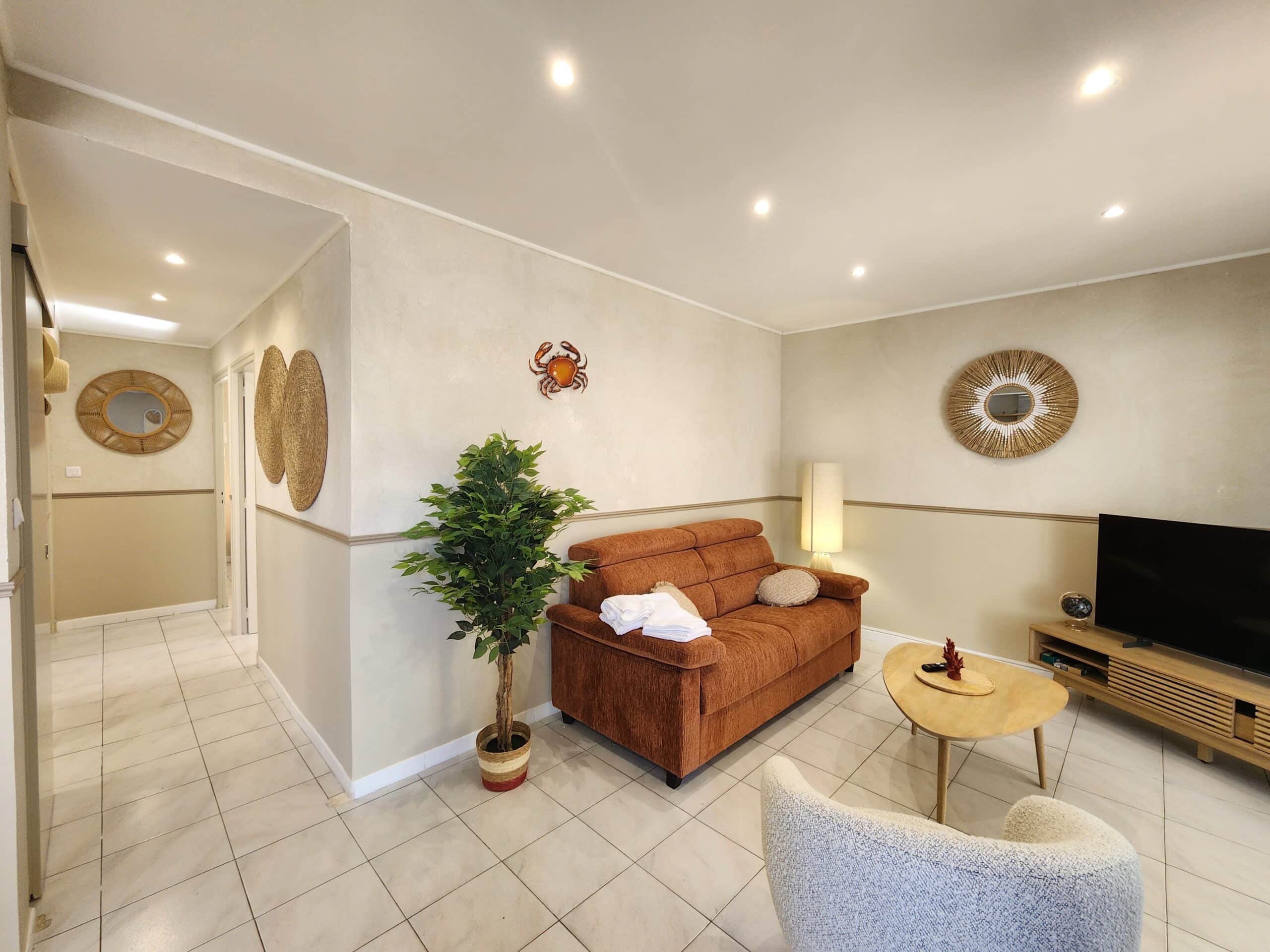 Salon moderne style côtier avec canapé brun, plante verte et miroirs en rotin sur murs beiges.