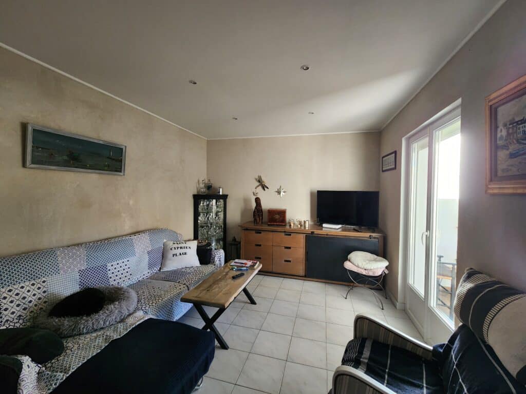 Salon avec canapé bleu, table bois et coussin 'SAINT CYPRIEN PLAGE'. Style rustique moderne et lumineux.