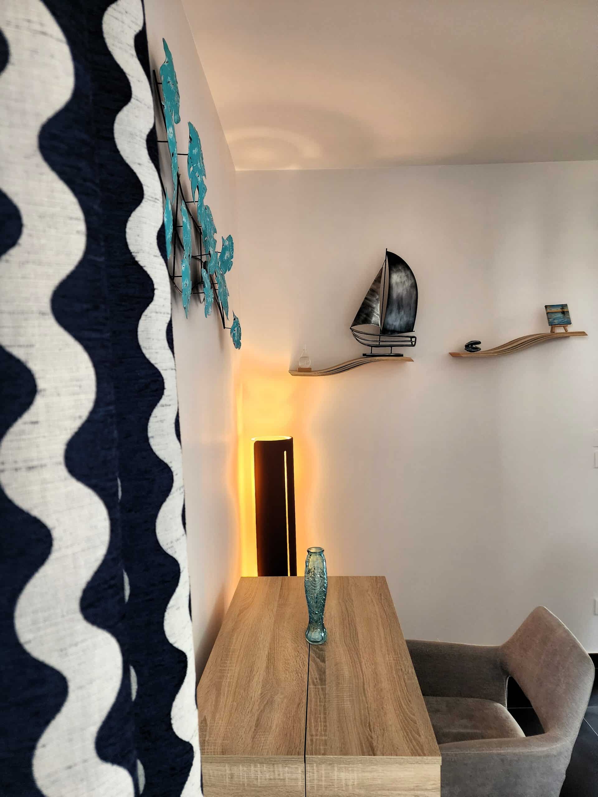 Bureau en bois avec vase bleu, décoration marine murale et rideau à vagues sous une lumière tamisée.