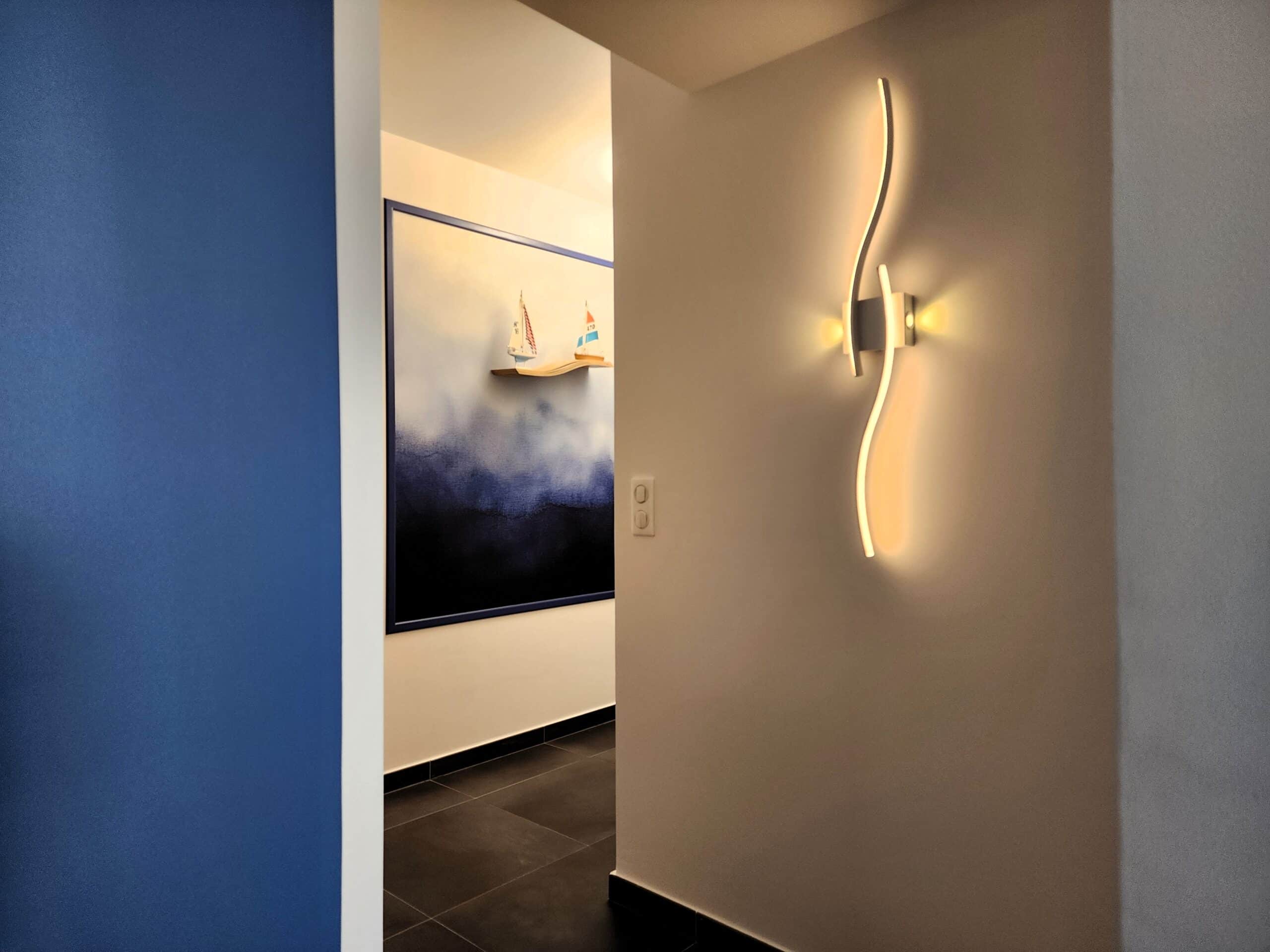 Décoration de couloir moderne avec applique murale design et tableau marin aux nuances de bleu et voiliers.