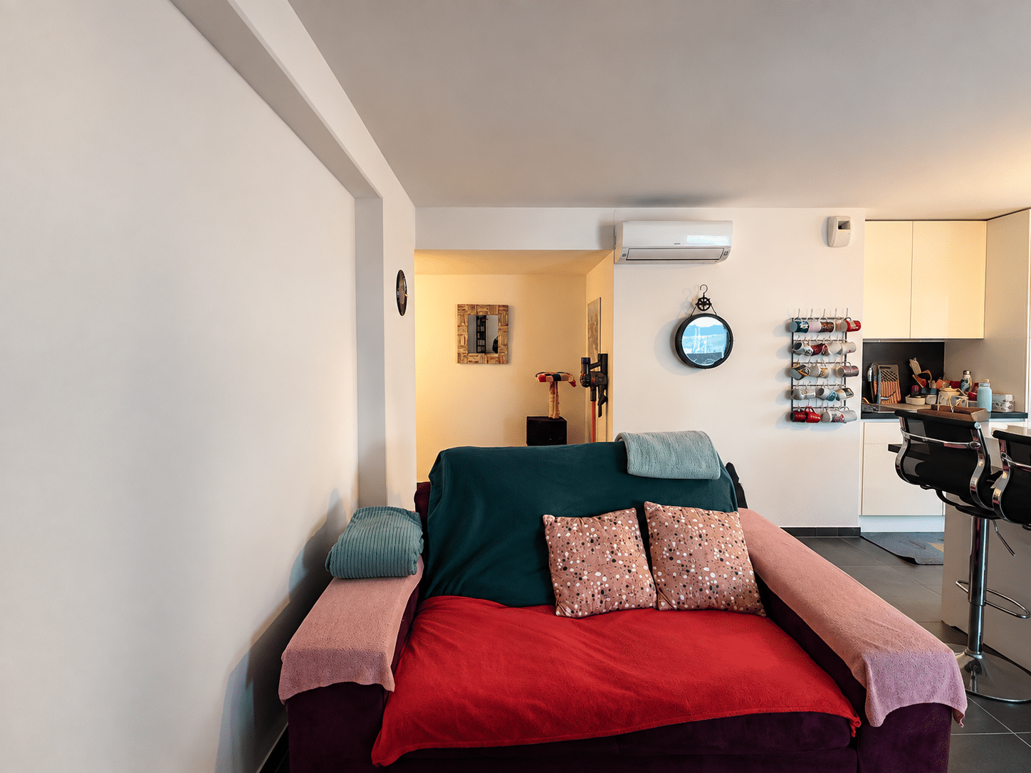Canapé coloré avec plaids et coussins, mur décoré d'un porte-tasses et miroir dans un salon moderne.