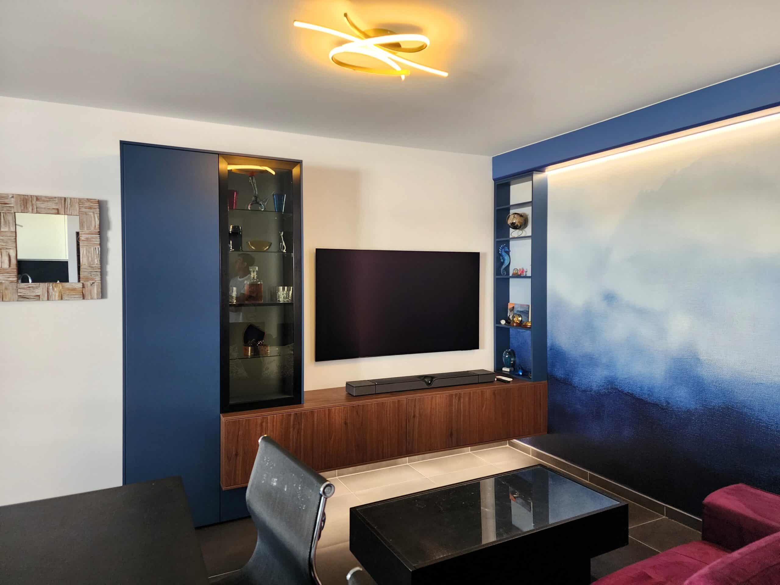 Salon moderne avec meuble TV bleu marine, murale artistique bleue et luminaire doré design au plafond.