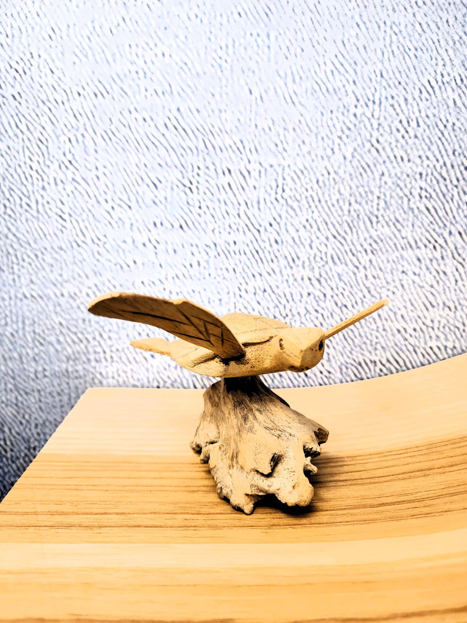 Sculpture artisanale d'une tortue volante en bois sculpté posée sur un socle de bois flotté rustique.