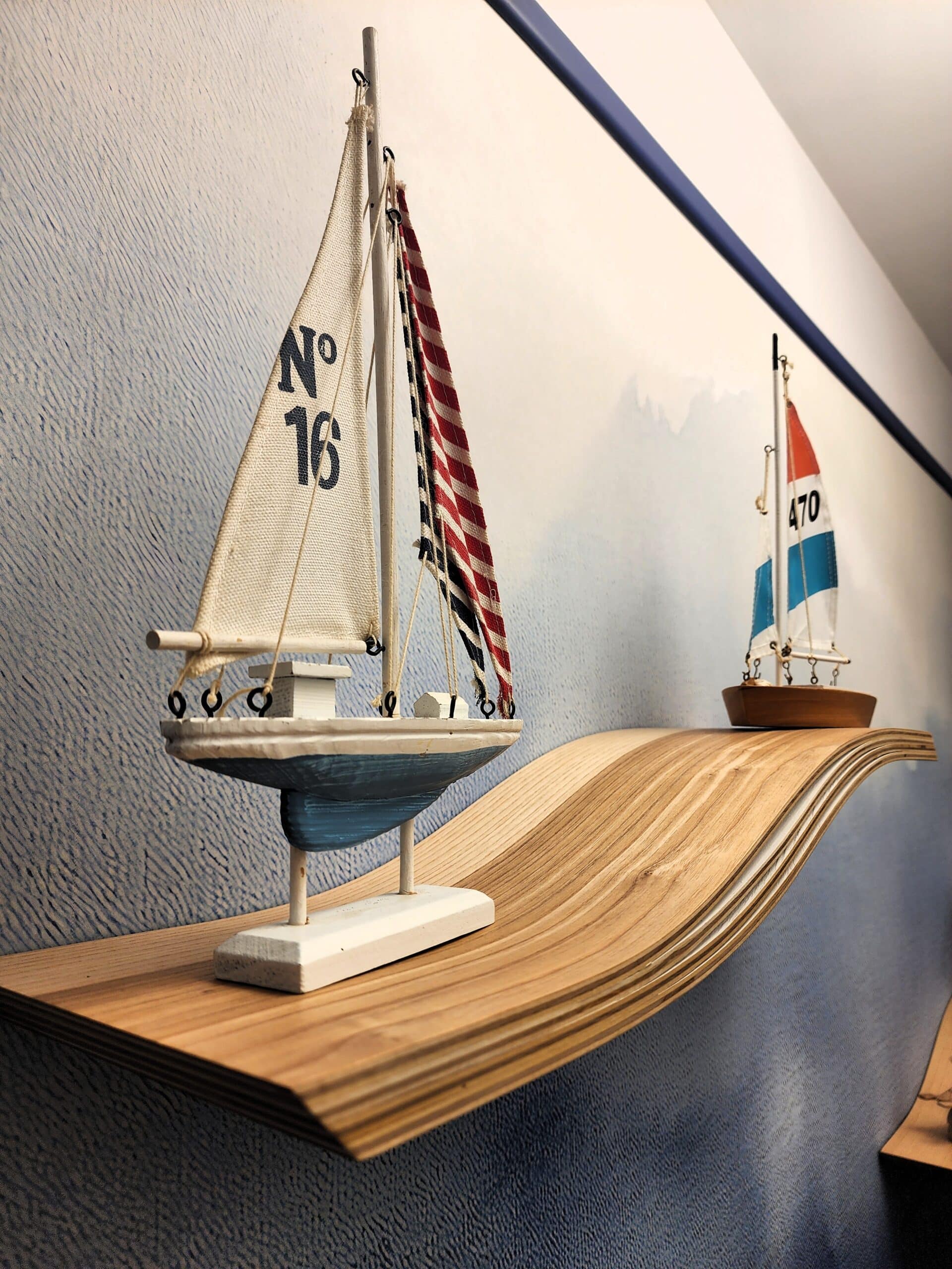Voiliers miniatures N° 16 et 470 sur une étagère en bois ondulée. Décoration marine sur mur bleu.